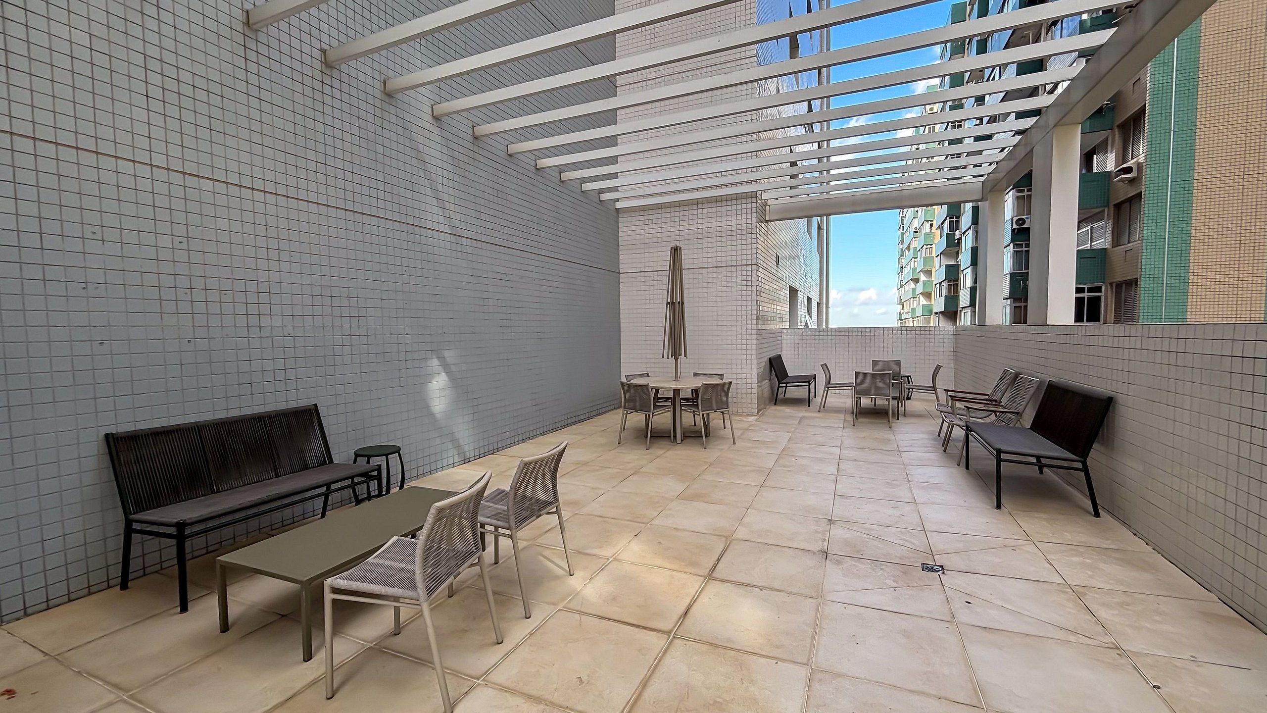 Un espace extérieur aménagé en terrasse, doté d’un sol carrelé, de tables et de chaises à structure métallique, et d’une pergola.