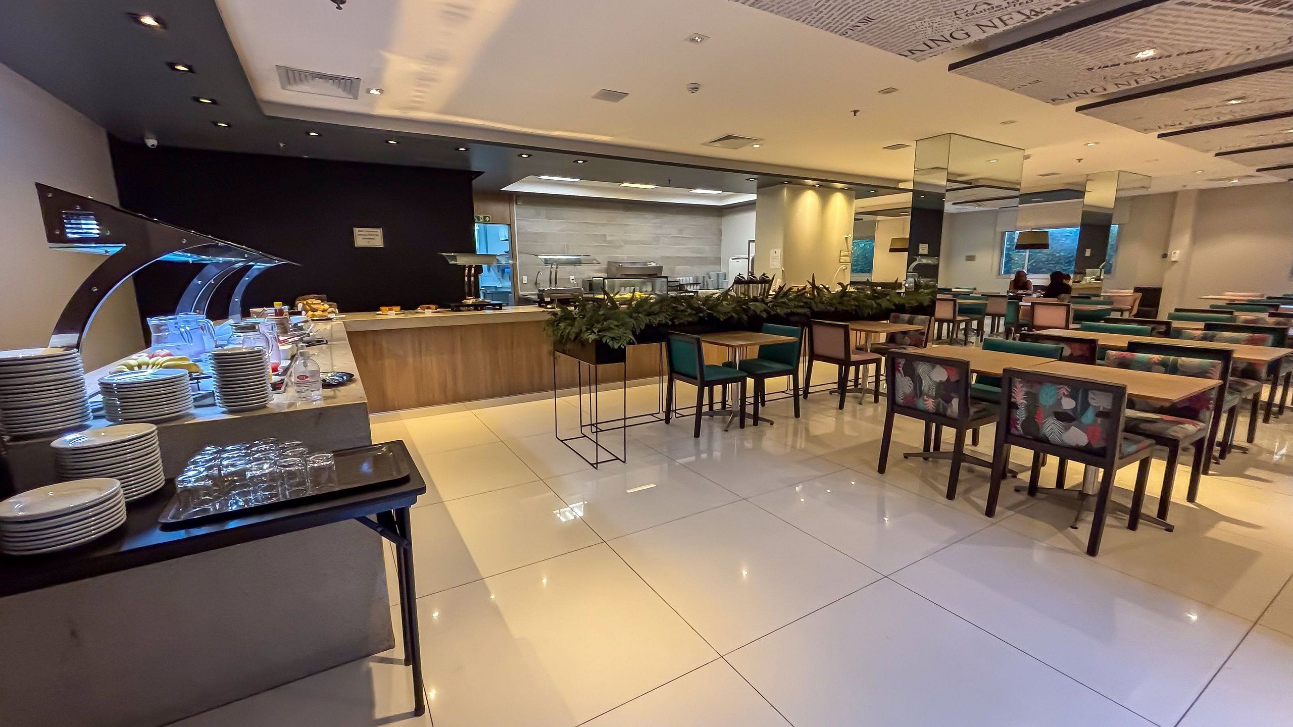 A modern restaurant with a buffet area, seating, and a kitchen in the background.