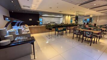 A modern restaurant with a buffet area, seating, and a kitchen in the background.