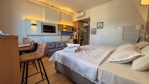 Quarto de hotel com cama, escrivaninha, cadeira, sofá e televisão.