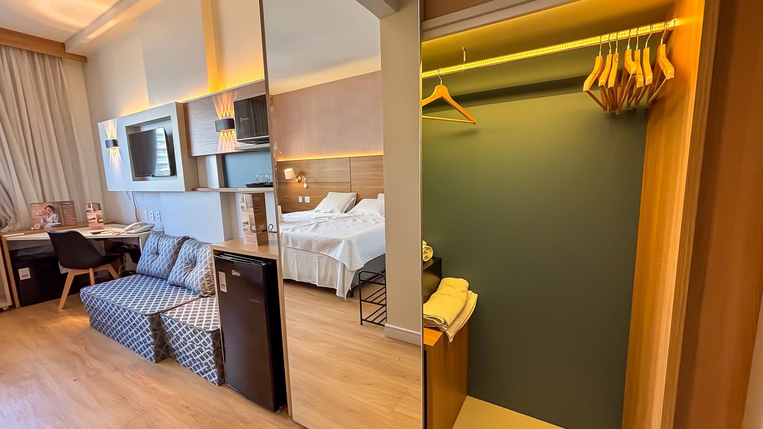 A hotel room with a bed, a desk, a TV, a mini-fridge, and a bathroom with a towel rack.