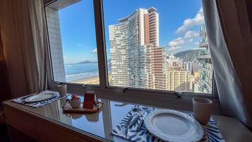 Habitación de hotel con un amplio ventanal con vistas a un paisaje urbano y una playa.
