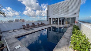 A rooftop pool with lounge chairs, a modern building with large windows, and a cityscape view. - SHB Gonzaga Lazer Completo 200m Praia (Santos)