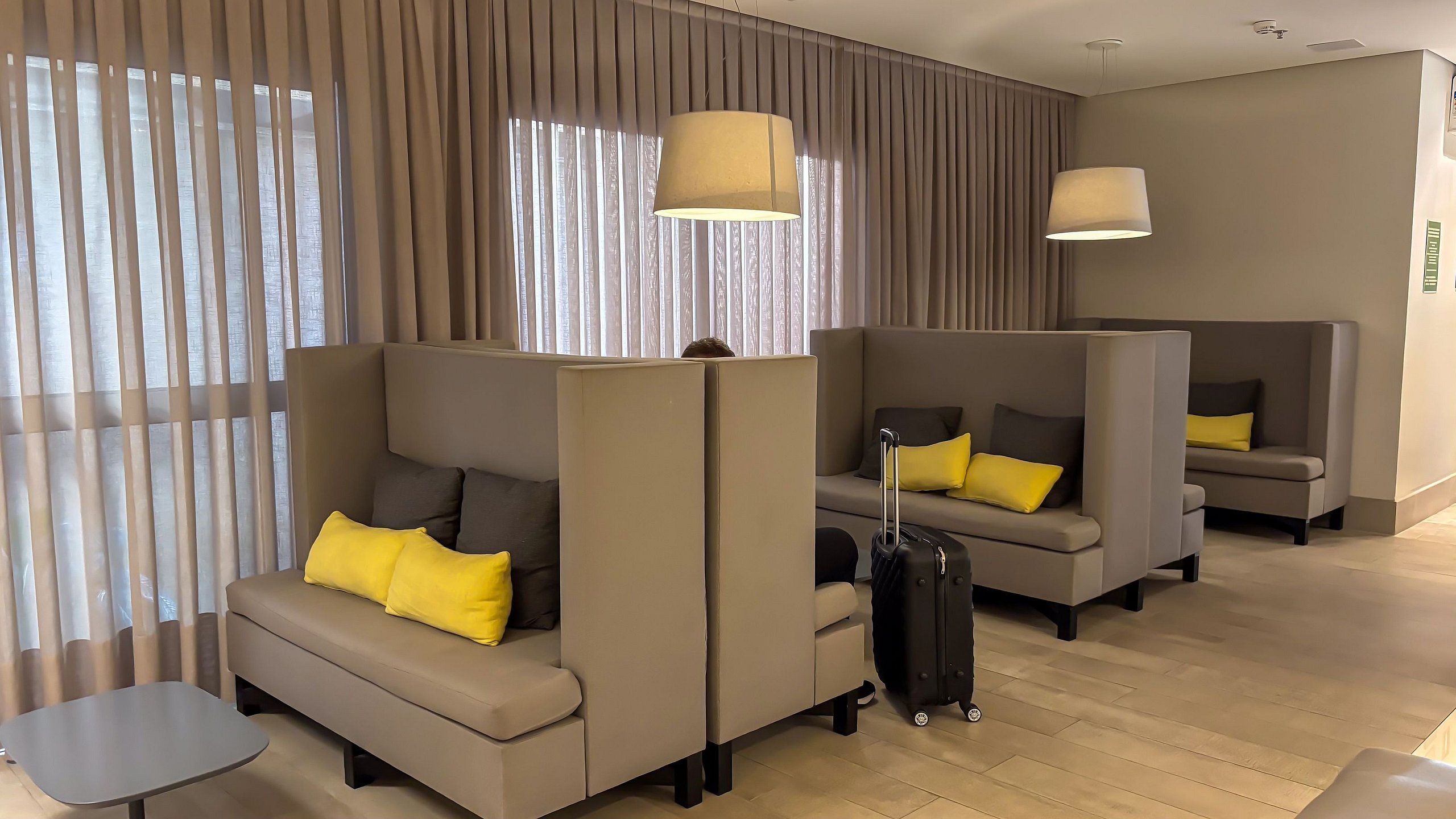 A hotel room with a sectional sofa, a small table, a suitcase, and a lamp.