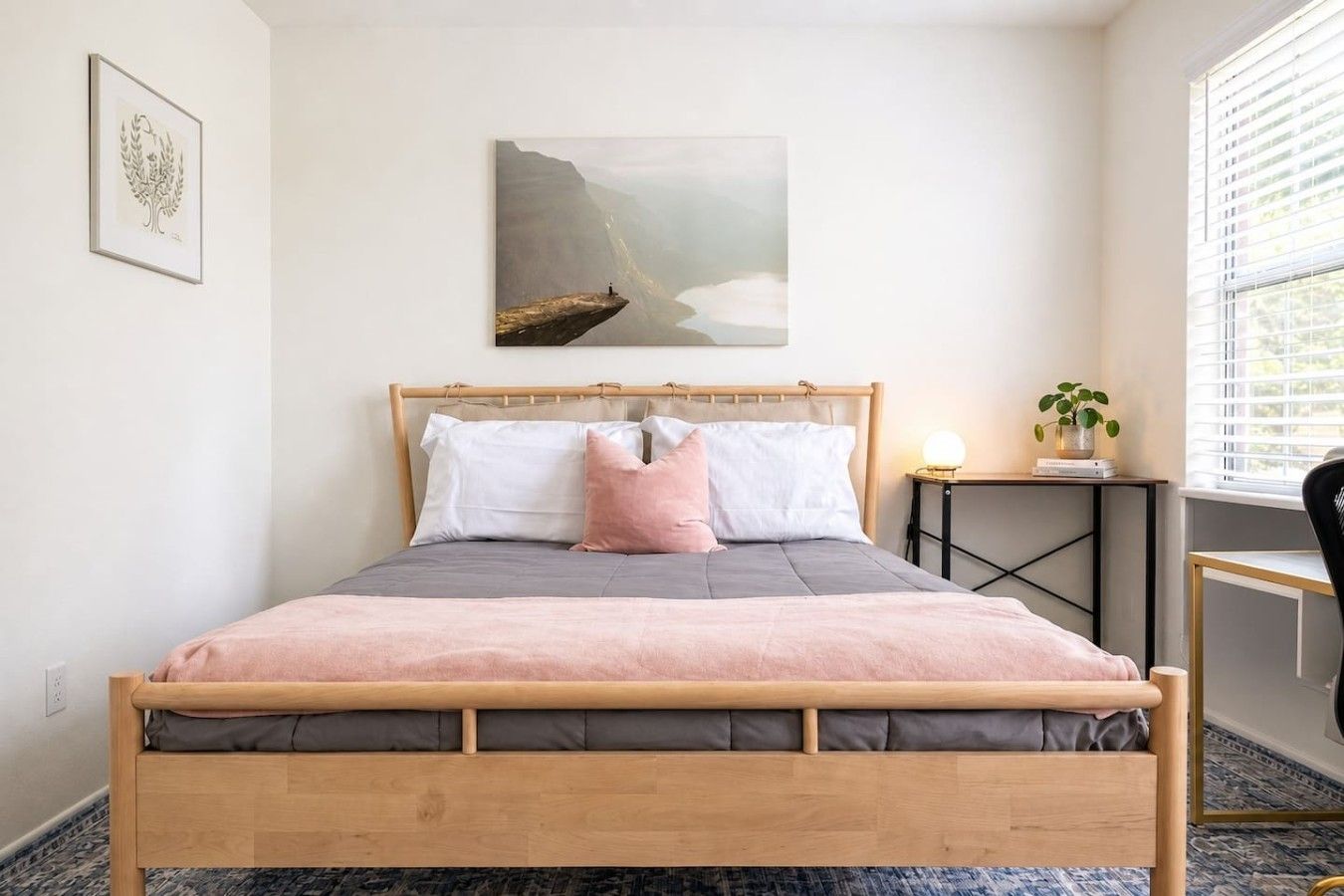 Une chambre à coucher avec un lit en bois, une table de chevet avec une lampe, une fenêtre avec des stores et un tableau accroché au mur.