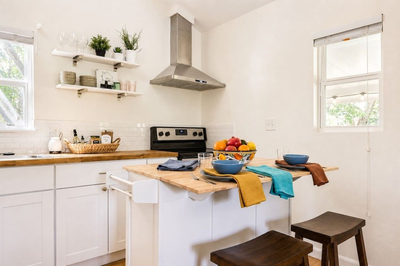 A modern kitchen with white cabinetry, a stainless steel range hood, and a wooden countertop.