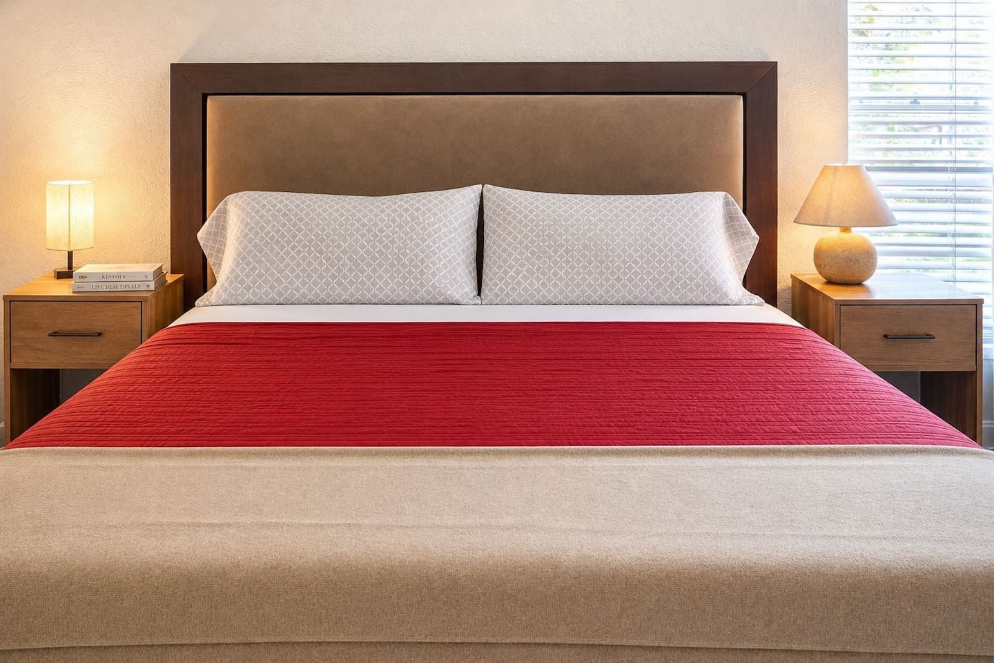 Ein Bett mit roter Bettdecke, zwei Kissen, einem Holz-Kopfteil und Nachttischen mit Lampen.