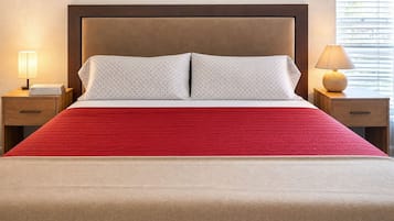 Een bed met een rode spreidek, twee kussens, een houten hoofdbord en nachtkastjes met lampen.