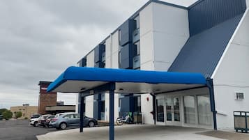 Un edificio moderno con acceso cubierto, un estacionamiento con varios coches y un cielo despejado.