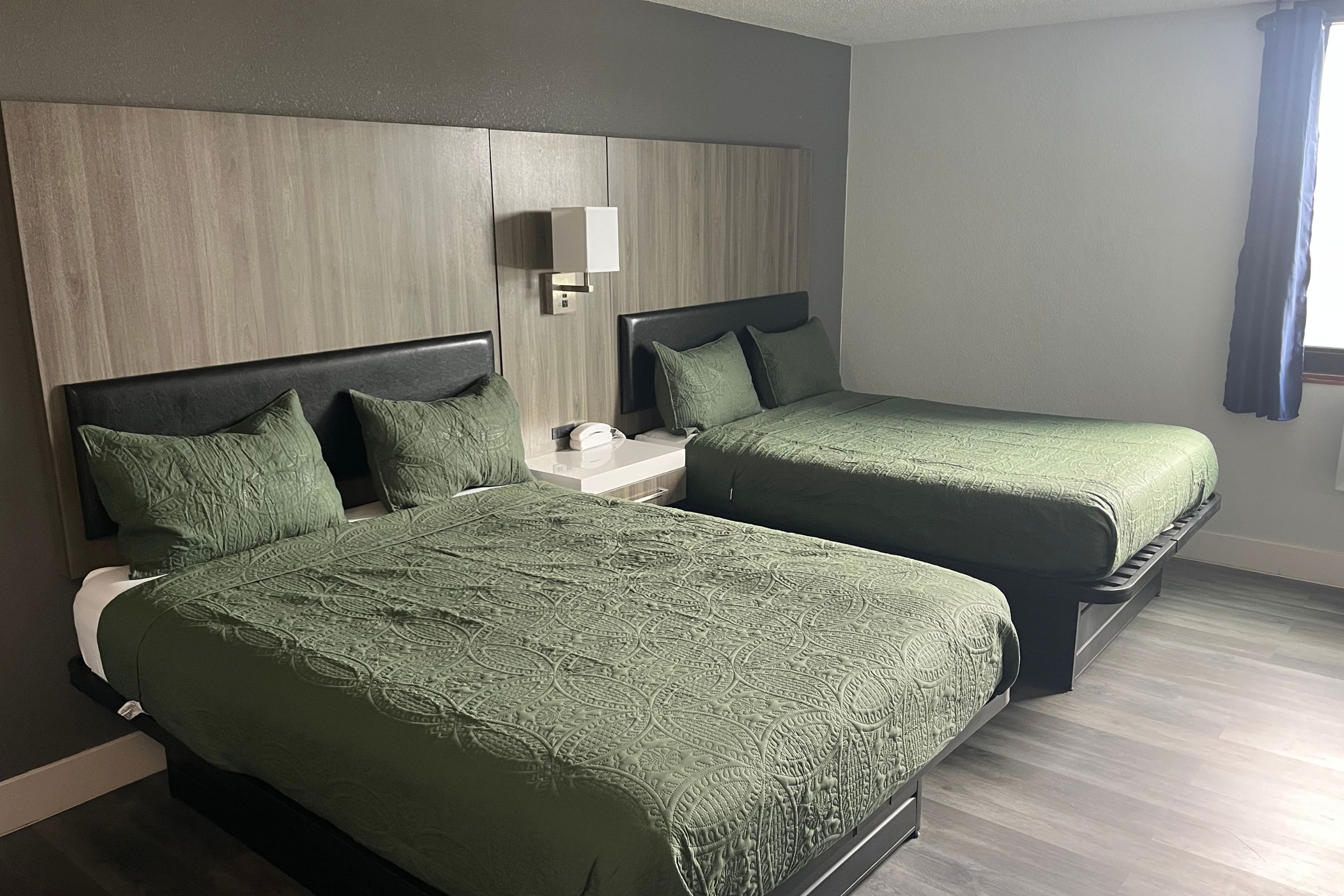 A hotel room with two beds, a nightstand, and a wall-mounted light.