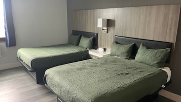 Habitación de hotel con dos camas, una mesita de noche y una lámpara fijada en la pared.