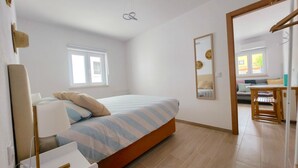 Een slaapkamer met een bed, een raam, een spiegel en uitzicht op een andere kamer.