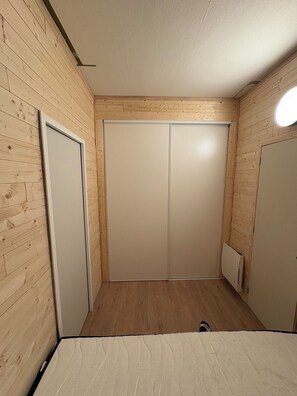 Ein Zimmer mit Holzwänden, einer weißen Tür und einem weißen Kleiderschrank mit Spiegel.