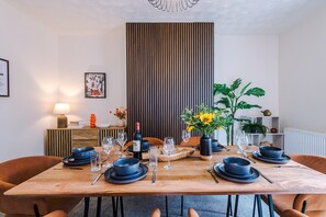 Un comedor con una mesa de madera preparada para una comida, flanqueada por sillas, con un panel de madera vertical y un cuadro en la pared.