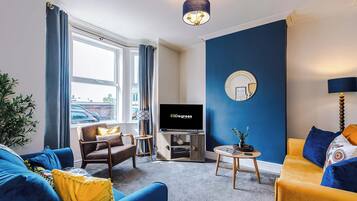 Ein modernes Wohnzimmer mit großem Fernseher, einer Couch, einem Sessel und einem Couchtisch.