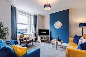 A modern living room with a large TV, a sofa, a chair, and a coffee table. - Stunning New Home in Hoole, Chester! Sleeps 6 (Chester)