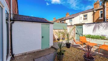 A residential courtyard with a white garage, green door, potted plants, and outdoor seating.