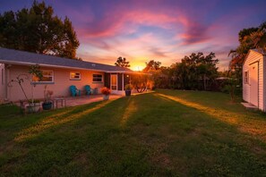Una propiedad residencial con un césped cuidado, un patio con mobiliario exterior y una casa con garaje visible.