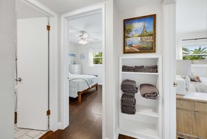 A bedroom with a bed, a ceiling fan, a window with a view, and a shelf with folded towels. - St Pete Getaway Near Beaches Fenced Yard (St. Petersburg)