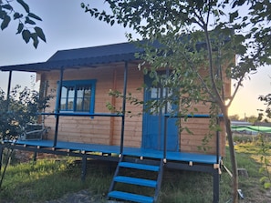 A wooden cabin with a blue door and window, a covered porch, and a small set of stairs leading up to the entrance.