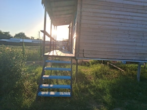 A wooden structure with a staircase leading to a covered area, surrounded by grass and a fence.