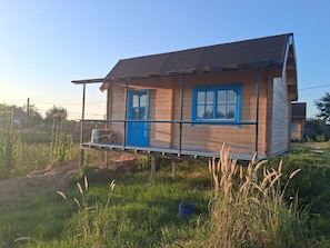 Een houten huis met een blauwe deur en ramen, verhoogd op palen en voorzien van een balkon.
