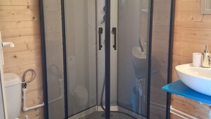 Kulmassa sijaitseva suihkukaappi, jossa on lasiovi, wc ja sinisellä tasolla varustettu pesuallas.