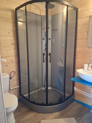 Douchecabine in hoek met glazen deur, toilet en wastafel met een blauw aanrechtblad.