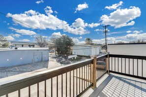 A view from a balcony overlooking a parking area with buildings, a fenced yard, and a clear sky. - Shipping Container Retreat | Modern Tiny Escape (Wichita)