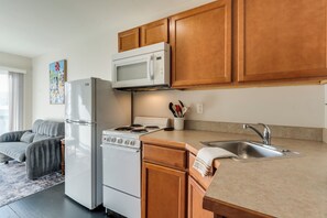 A compact kitchen with a refrigerator, microwave, stove, and wooden cabinets. - Shipping Container Retreat | Modern Tiny Escape (Wichita)