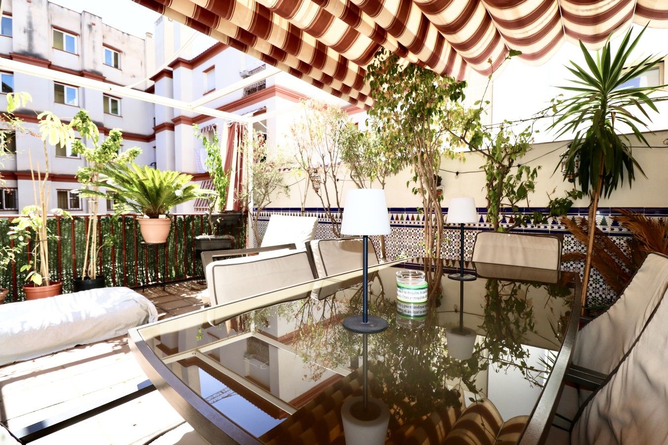 A sunlit outdoor seating area with a glass table, chairs, and potted plants.