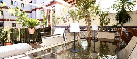 A sunlit outdoor seating area with a glass table, chairs, and potted plants.