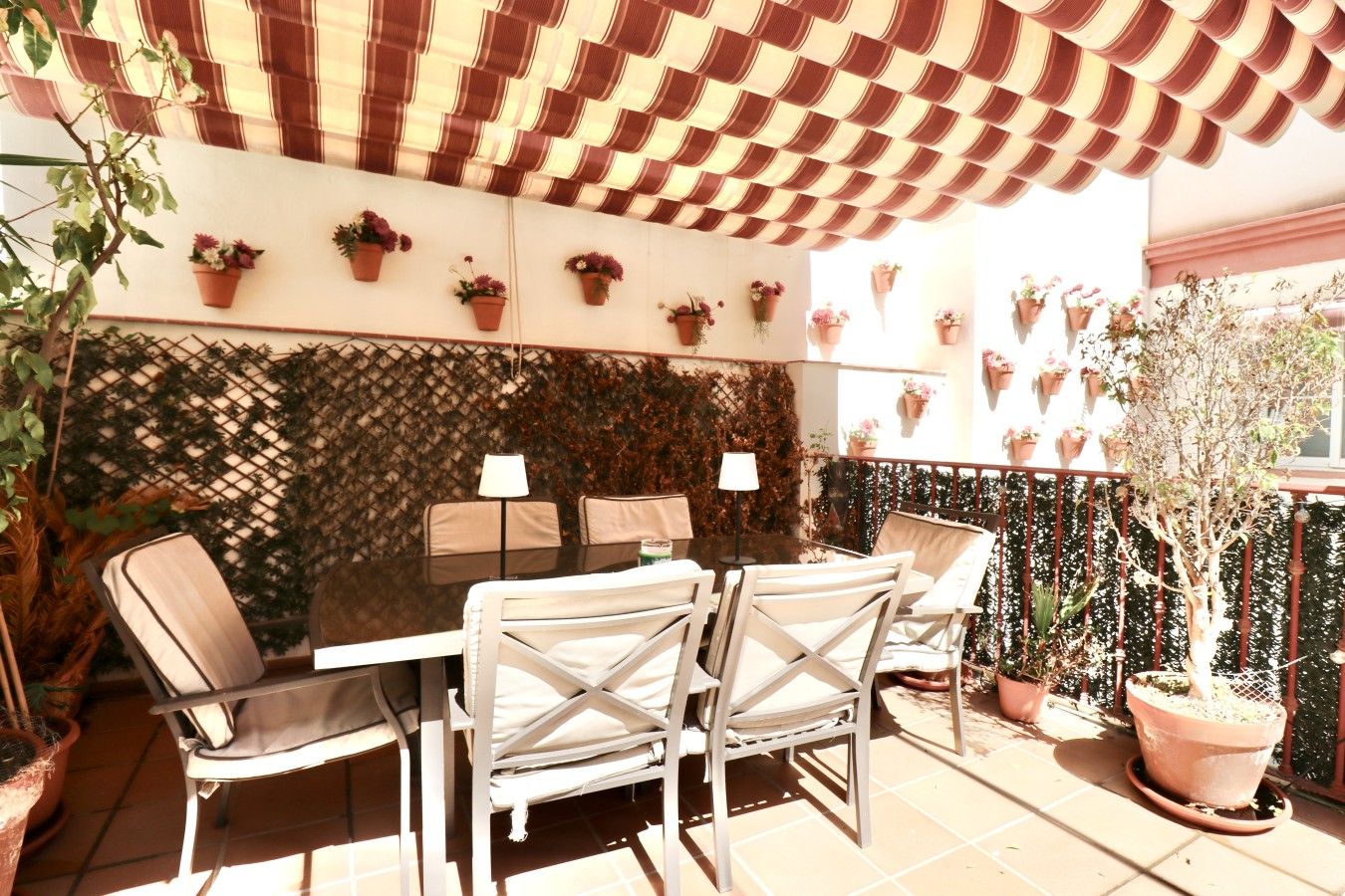 An outdoor patio with a table and chairs, surrounded by potted plants and a lattice wall.