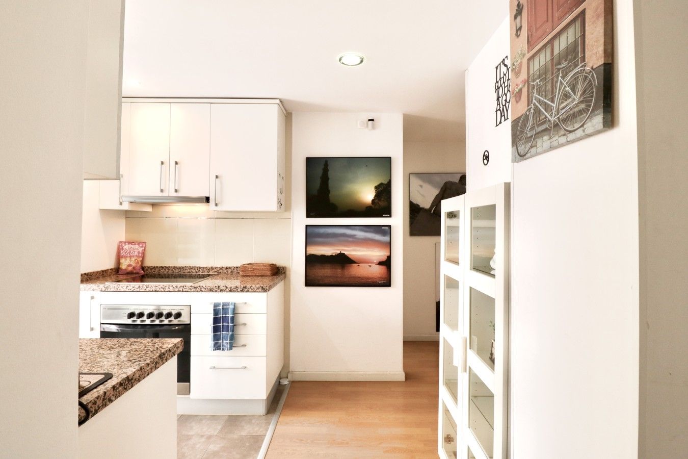 A kitchen with white cabinets, a granite countertop, and a stove. There are two framed pictures on the wall.