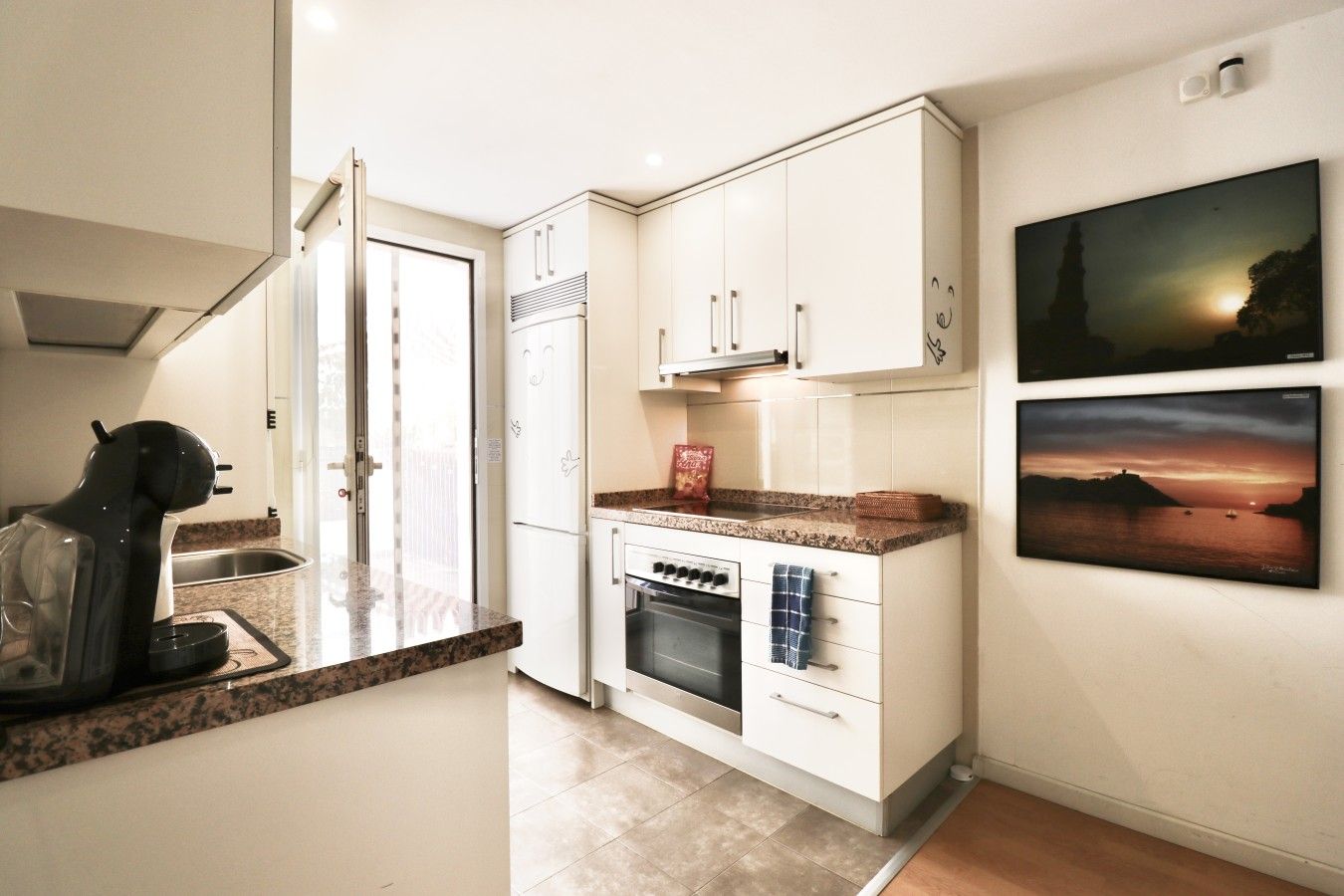 Una cucina moderna con mobili bianchi, forno integrato e un piano di lavoro con macchina da caffè.