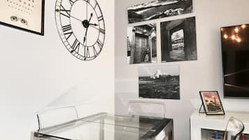 Une pièce avec une table en verre, des chaises, une horloge murale et des photographies encadrées.