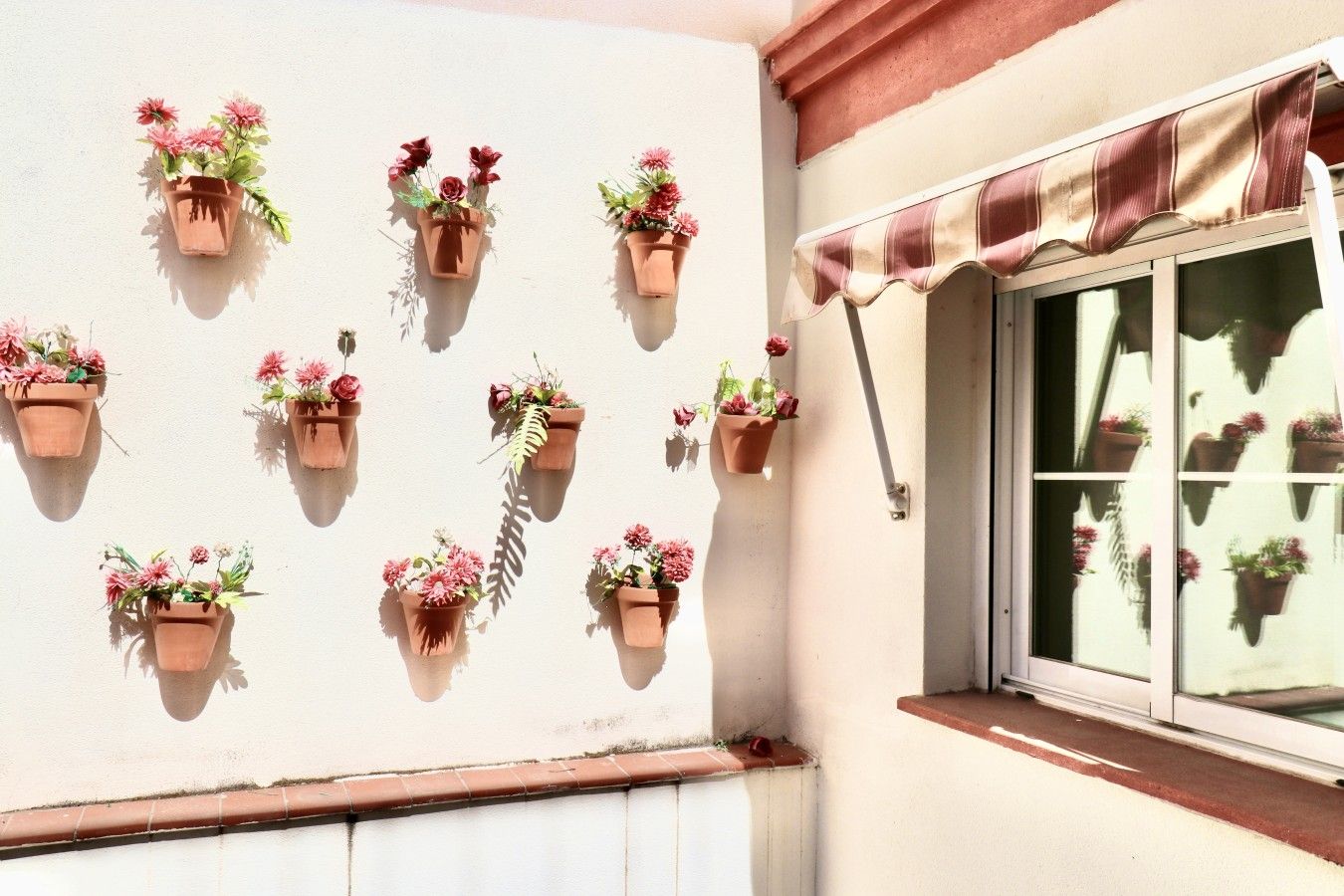 Ein Gebäudefassaden mit mehreren hängenden Blumenkästen und einem Fenster mit Markise.