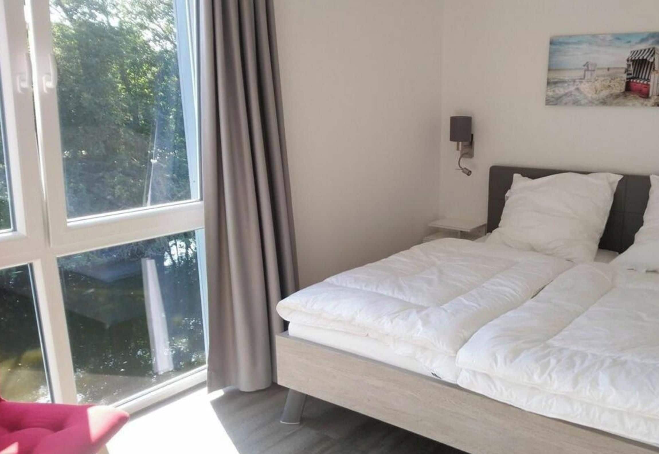 A bedroom with a bed, a window, and a painting on the wall.