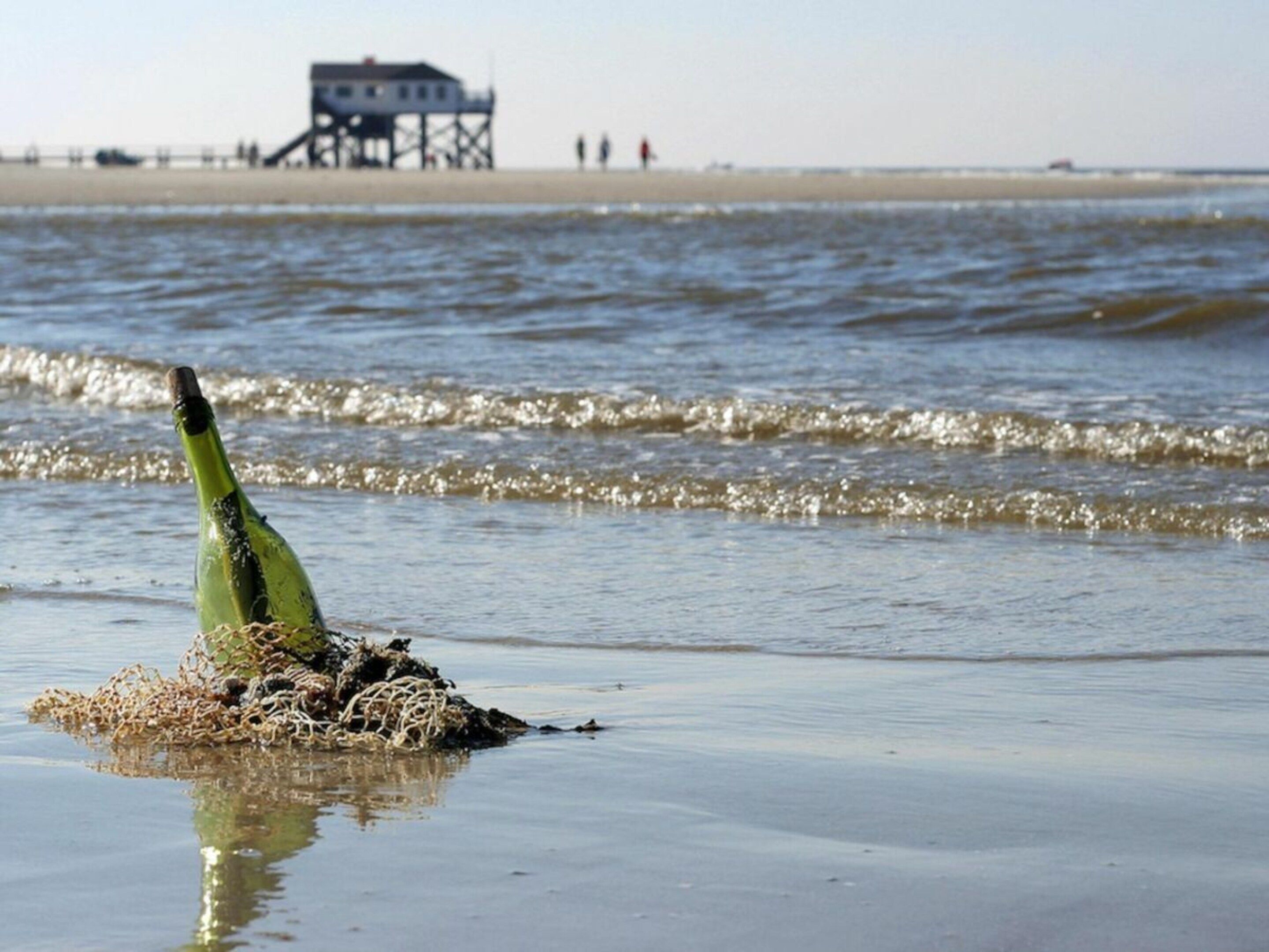 Eine Flasche am Strand, im Hintergrund Wellen.