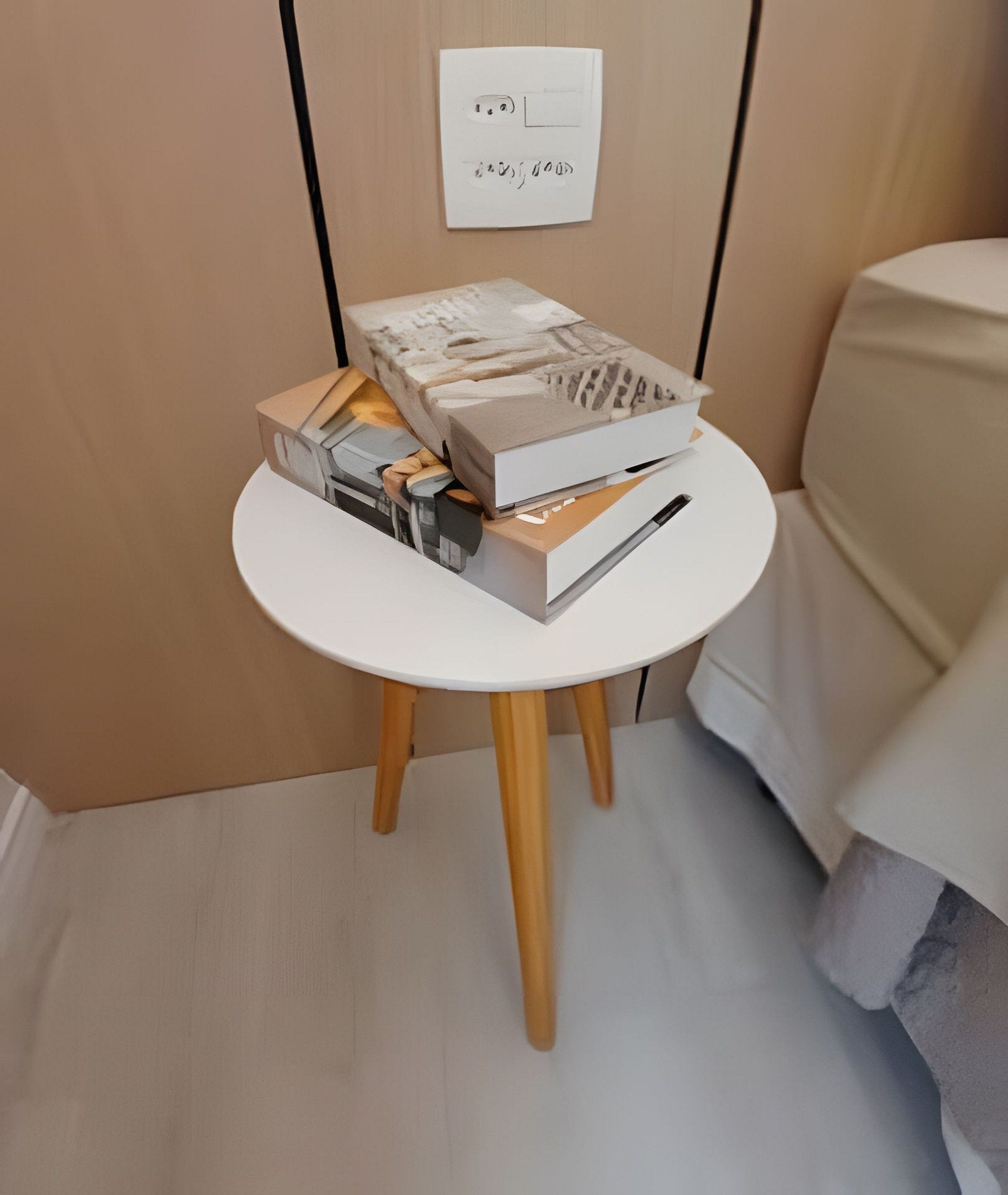 Een klein, rond tafeltje met een witte tafelblad en houten poten, waarop boeken en een klein doosje staan.