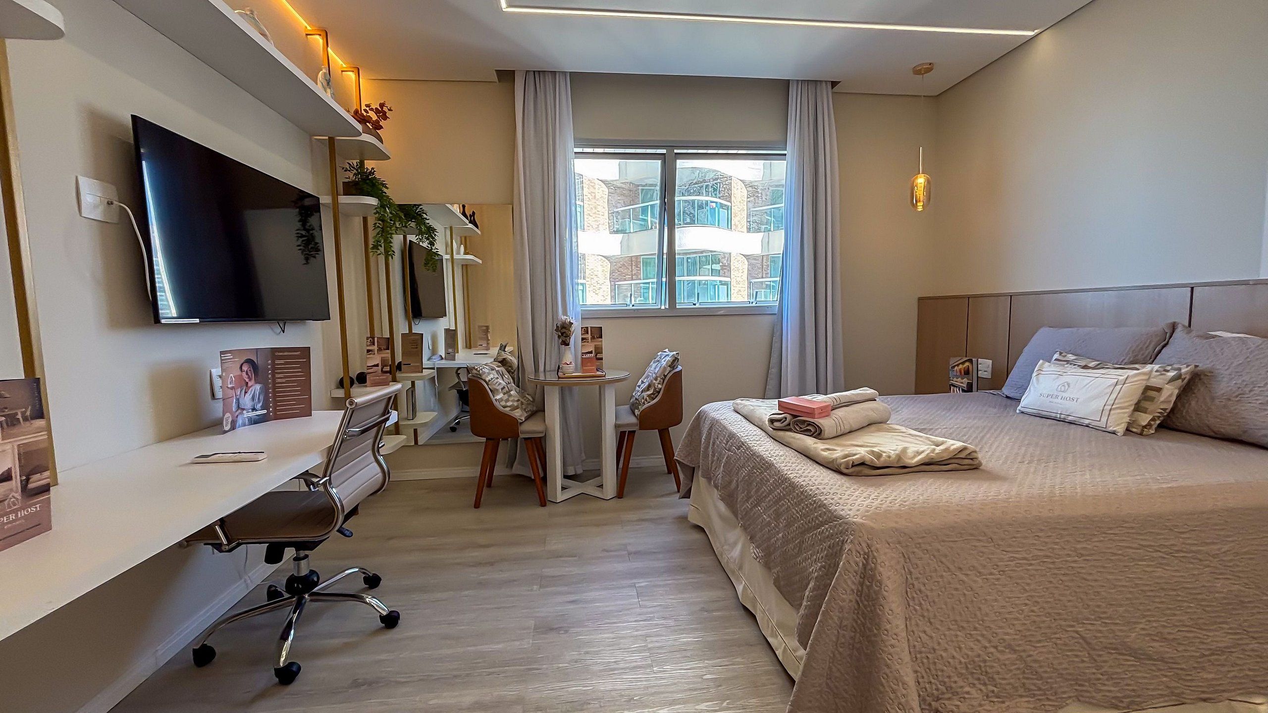 Una habitación de hotel con cama, escritorio, silla, televisor y ventana con vistas a edificios.