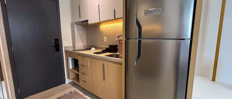 A compact kitchen with a refrigerator, a sink, and wooden cabinets.