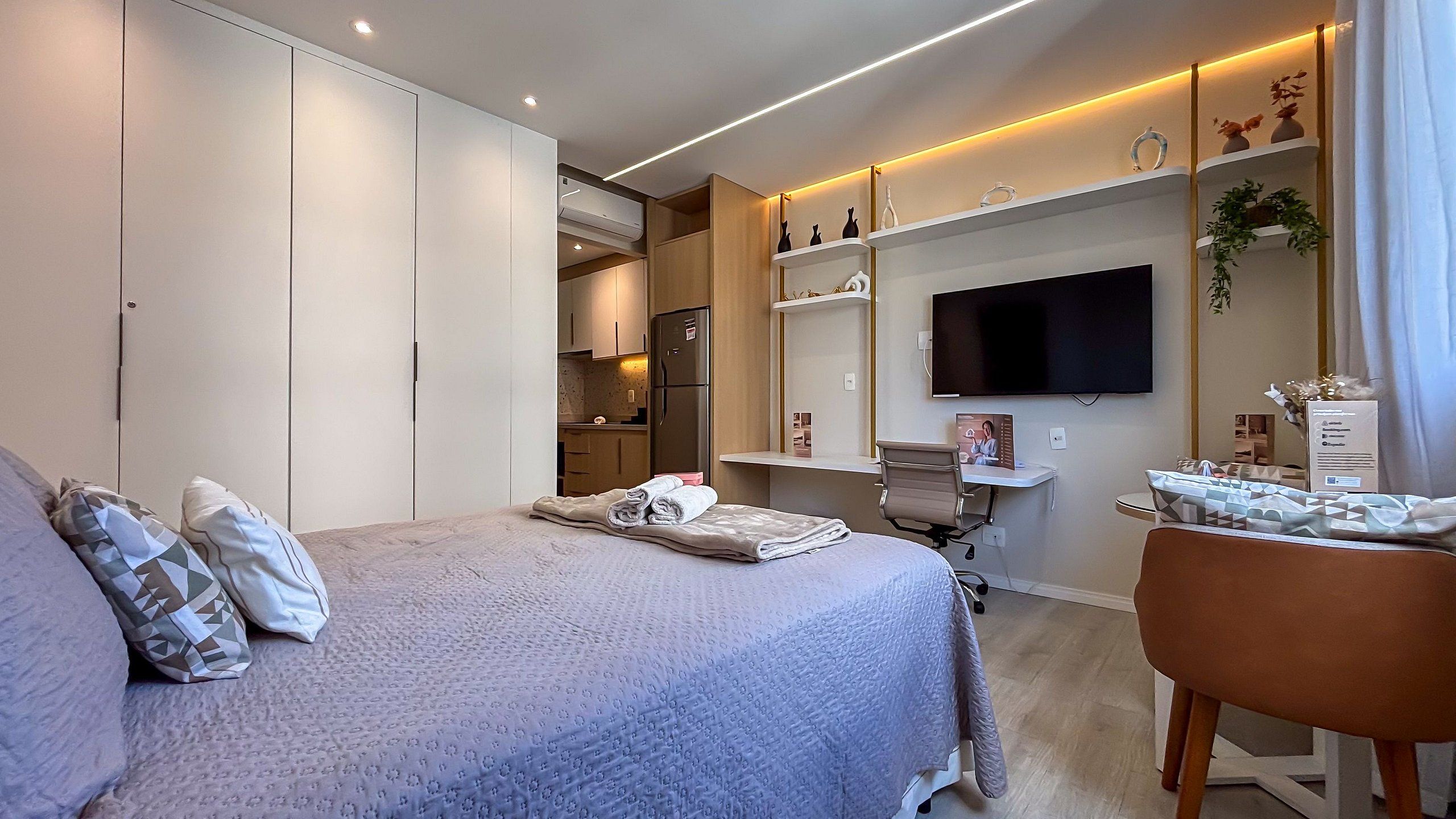 Una habitación de hotel moderna con una cama grande, un escritorio, un televisor de pantalla plana y una kitchenette.