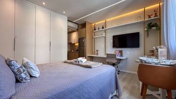 Una habitación de hotel moderna con una cama grande, un escritorio, un televisor de pantalla plana y una kitchenette.