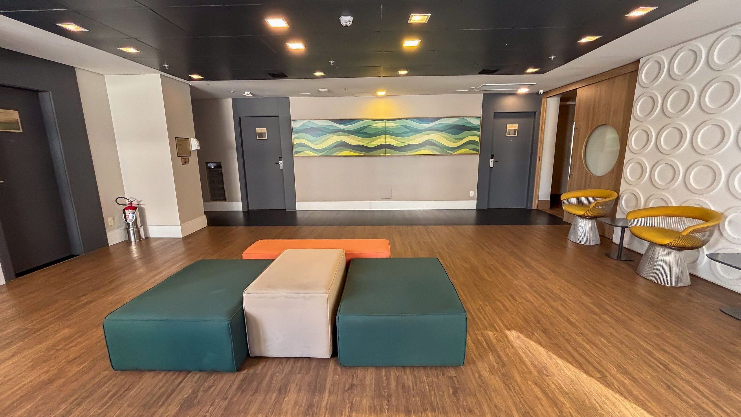 Un hall con mostrador de recepción, un área de estar con bancos acolchados y una pared con un diseño abstracto y colorido.
