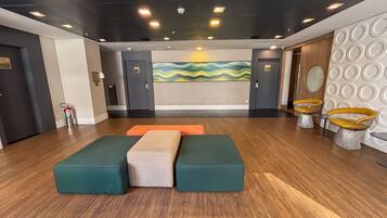 Un hall con mostrador de recepción, un área de estar con bancos acolchados y una pared con un diseño abstracto y colorido.