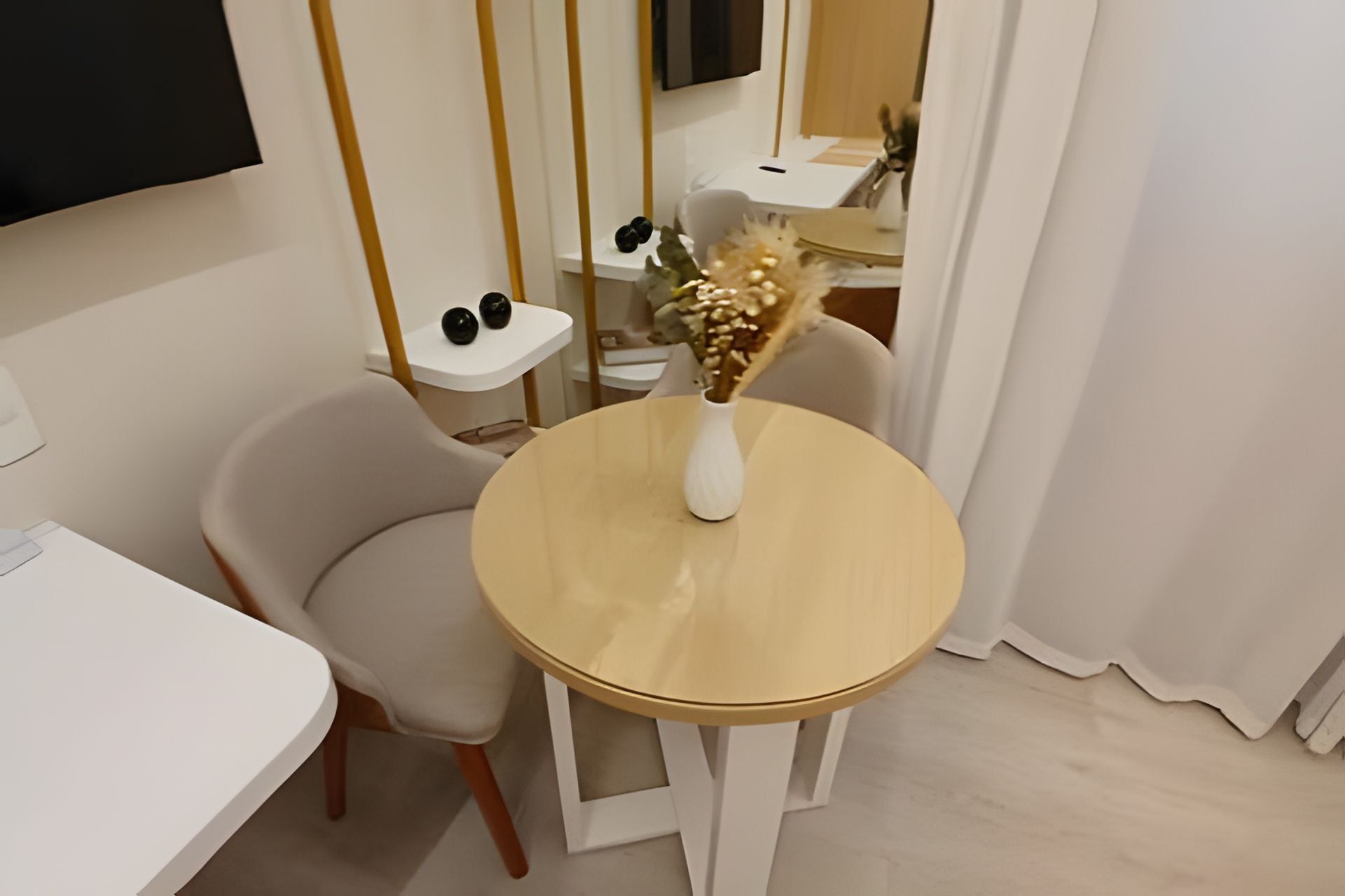 Un comedor moderno con una mesa redonda, una silla blanca y un jarrón con flores secas.
