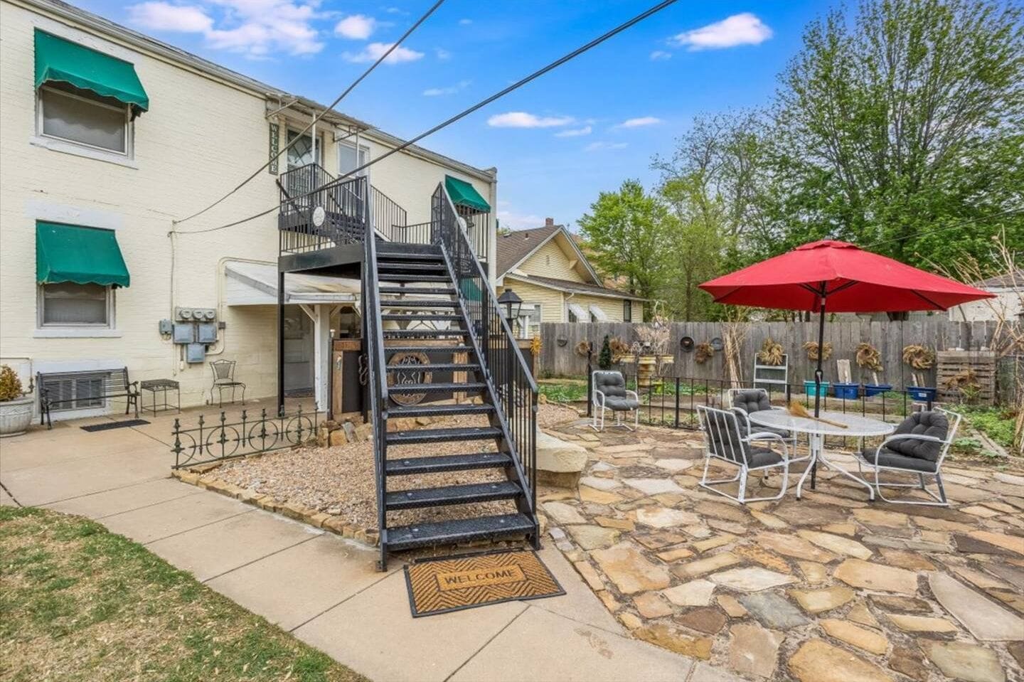 Private stone patio with outdoor seating, shade umbrella, and fenced yard