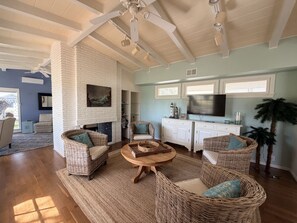 A spacious living room with a fireplace, wicker furniture, and a kitchen area with cabinets and a TV. - Journey by the Sea ~ Rockport, Texas (Rockport)