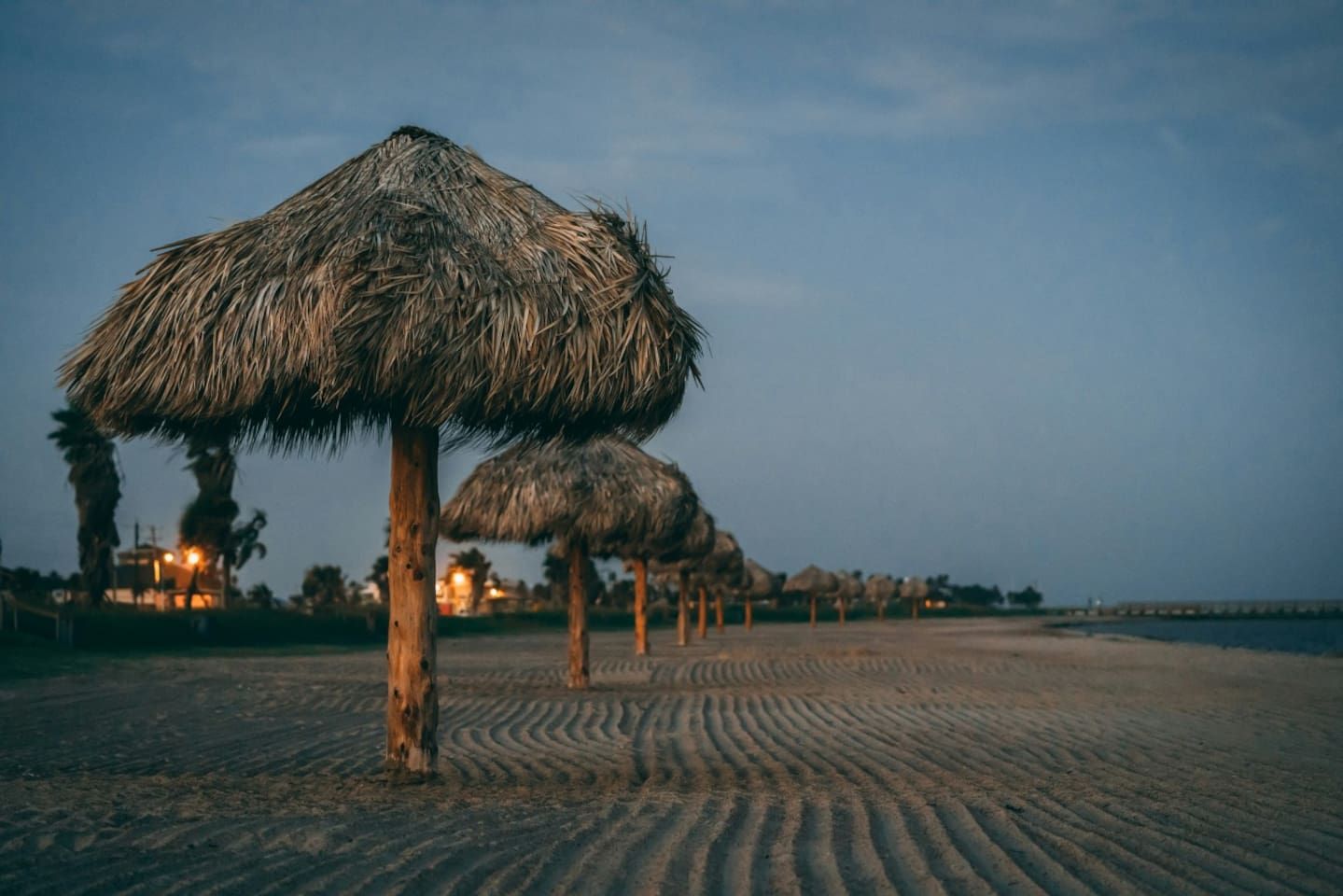 Ein Strand mit Reetsonnenstühlen und Palmen.